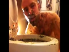 A naughty guy using his tongue to wipe a toilet bowl full of shit
